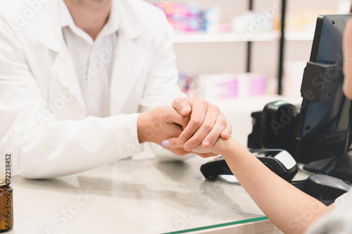 Cropped closeup shot of male druggist pharmacist doctor supporting  sympathizing female customer client buyer  listening attentively to her medical complaints at cash point desk