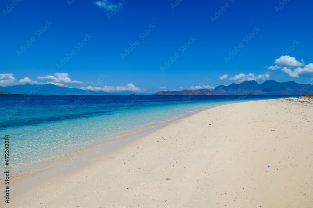 A view on white sand beach on a small island near Maumere, Indonesia. Happy and careless moments. Waves gently washing the shore. Clear, turquoise coloured water displaying coral reef. Hidden gem.