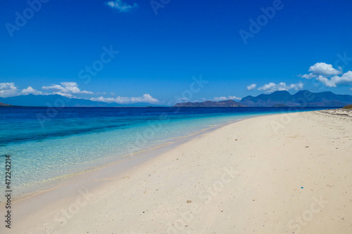 A view on white sand beach on a small island near Maumere, Indonesia. Happy and careless moments. Waves gently washing the shore. Clear, turquoise coloured water displaying coral reef. Hidden gem.