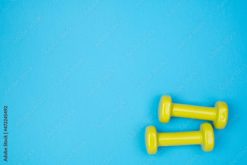 Yellow dumbbells on blue background, top view with copy space Yellow dumbbells on blue background, top view with copy space