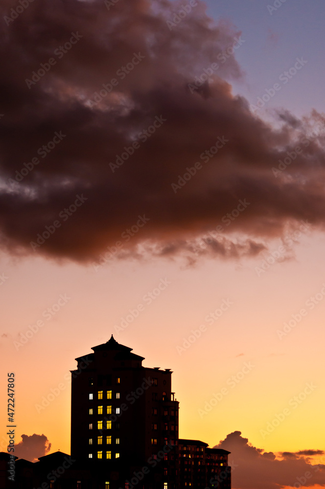 front view, far distance of a silhouetted building, at dusk, just before sunset, with a thunder cloud over the top