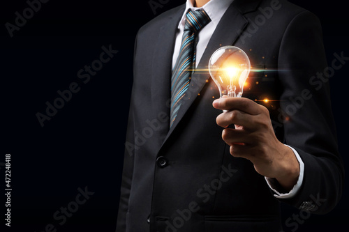 businessman investor in black suit hand holding vintage light bulb with light on dark background, business marketing, technology, inspiration, innovation, digital, internet, communication concept