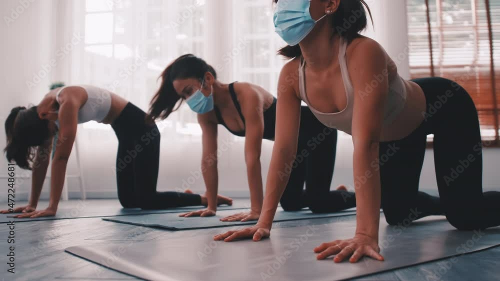 A group of Asian women wearing medical masks while doing yoga exercise at gym. A group of Asian women wearing medical masks while doing yoga exercise at gym.