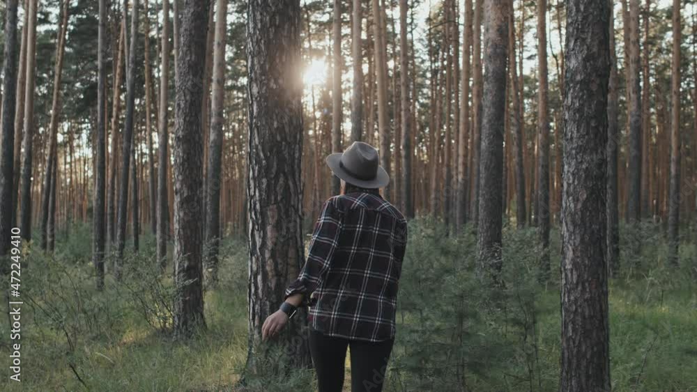 Handheld tracking shot of young woman in hat walking through forest on sunny summer day Handheld tracking shot of young woman in hat walking through forest on sunny summer day