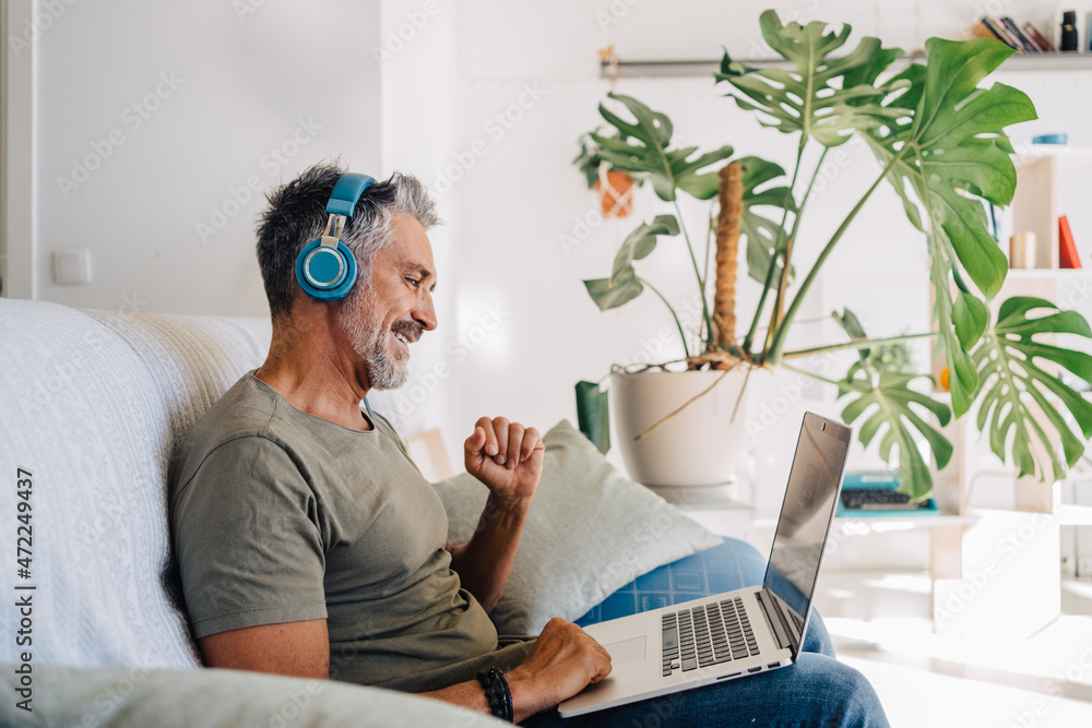 Aged man on couch enjoying music from laptop Aged man on couch enjoying music from laptop