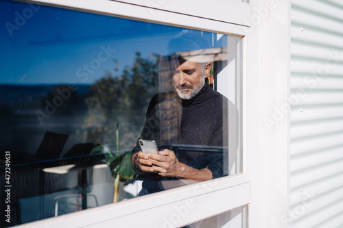 Aged male using mobile phone behind glass window