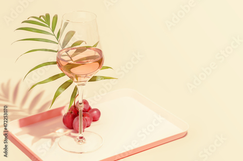 The concept of a tropical holiday resort and relax. Drink composition with a glass of rose wine with palm leaf and grape on a pink background with copy space. Summer party. Selective focus photo