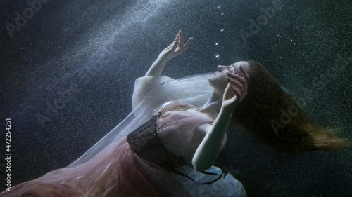 a charming young woman keeps afloat under the water in the ocean in a dress magical and fantastic