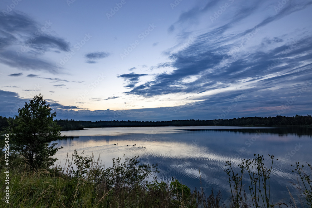 a beautiful blue lake with green tree in the foreground under a dramatic blue dusk sky. High quality photo