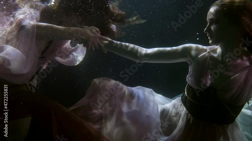 two charming mermaids are swimming underwater in dresses. homosexual relations between women