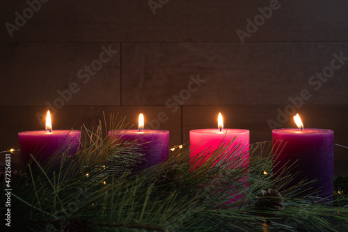 Four candles lit in advent wreath for fourth week of advent with pillar candles on dark wood