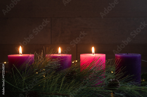 Three candles lit in advent wreath for third week of advent with pillar candles on dark wood