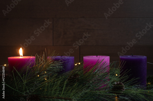 Single candle lit on advent wreath for first week of advent with pillar candles, wood background and copy space