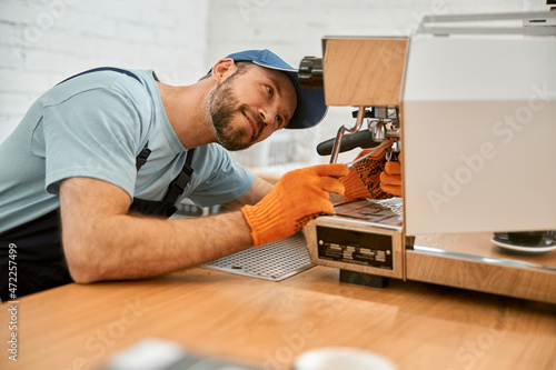 Smiling young man fixing coffee machine in cafe