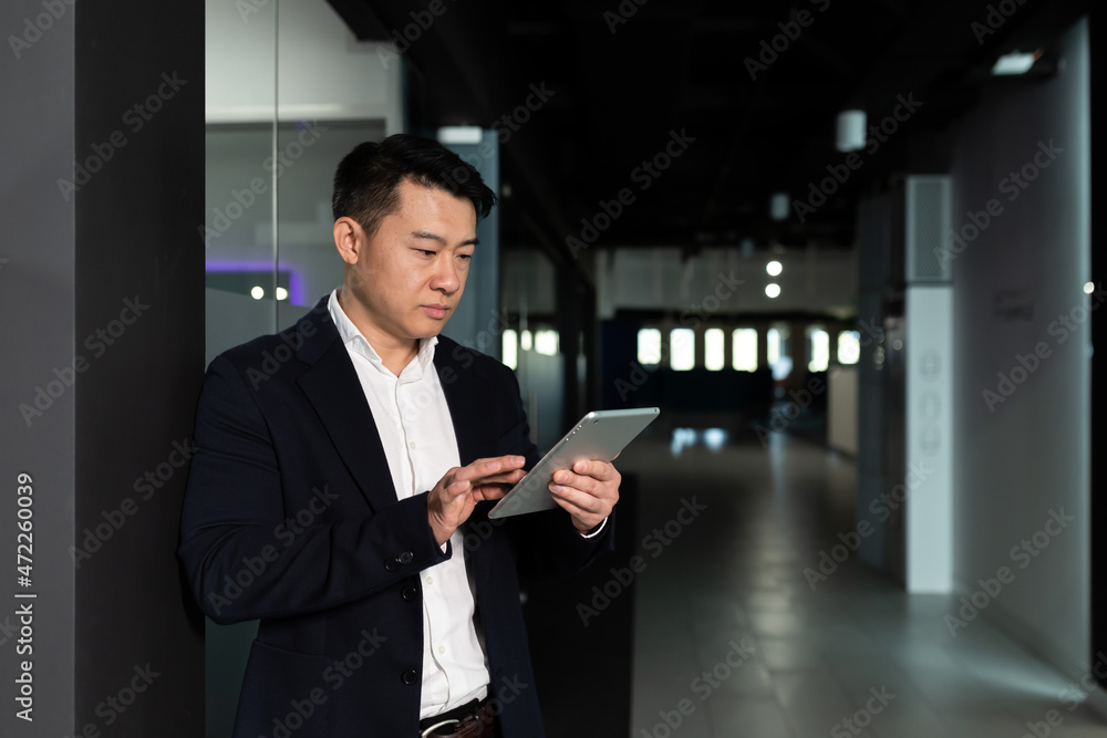 Fototapeta premium Serious asian male worker focused on work working with tablet computer in modern office