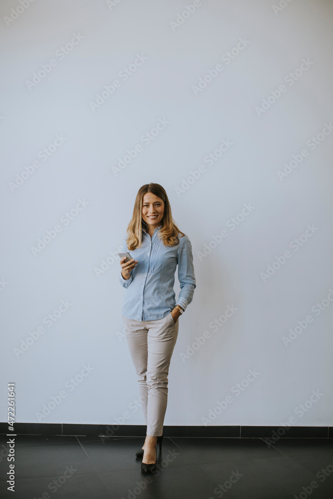 Business woman using mobile phone by the wall in the office Business woman using mobile phone by the wall in the office