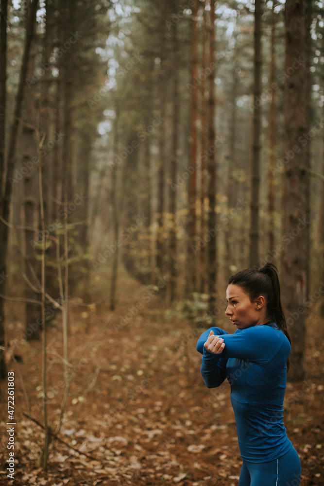 Young woman in blue track suit stretching before workout in the autumn forest Young woman in blue track suit stretching before workout in the autumn forest