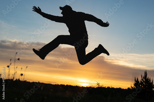 male silhouette of a jumping man on the way up, background sky during sunset