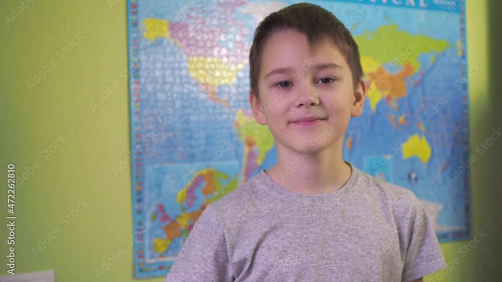 a teenager drinks water from a glass. then he looks at the camera and smiles. a political map of the world hangs on the background of the wall a teenager drinks water from a glass. then he looks at the camera and smiles. a political map of the world hangs on the background of the wall