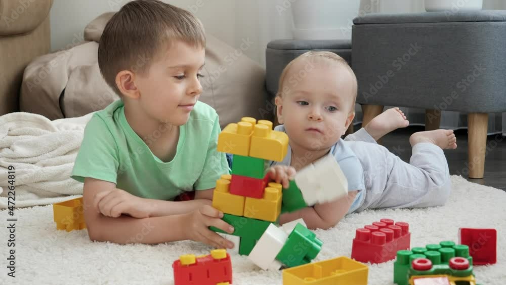 Little boy teaching his baby brother building tower with toy blocks and bricks. Concept of children development, education and creativity at home Little boy teaching his baby brother building tower with toy blocks and bricks. Concept of children development, education and creativity at home