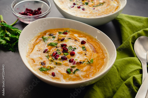 Bowls of Moroccan Roasted Pumpkin Soup: Roasted pumpkin soup garnished with mint leaves, pomegranate seeds, and chopped pistachios