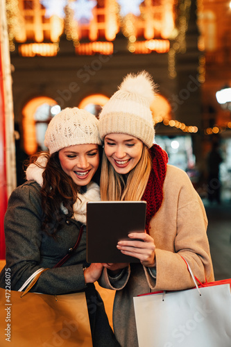 Happy women friends enjoying shopping together outdoors. People christmas shopping tablet concept