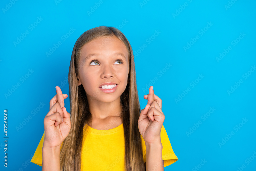 Photo of nervous little lady crossed fingers look empty space wear yellow t-shirt isolated blue color background Photo of nervous little lady crossed fingers look empty space wear yellow t-shirt isolated blue color background