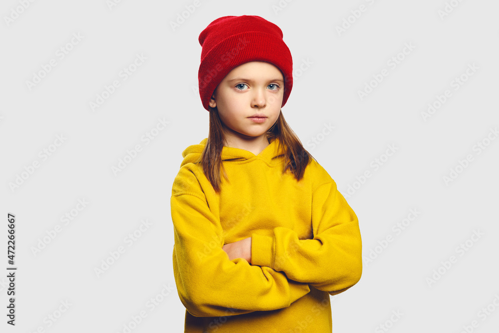 Serious looking offended kid, keeps hands crossed, has gloomy upset expression, has complains, wears yellow sweatshirt, isolated over white background