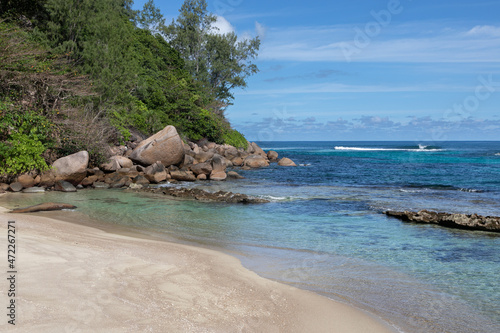 Sandy beach with huge rock, stones and hill covered with rainforest in the end. Fossilized corals in the crystal blue water. This is the Anse Consolation beach in the Seychelles. 