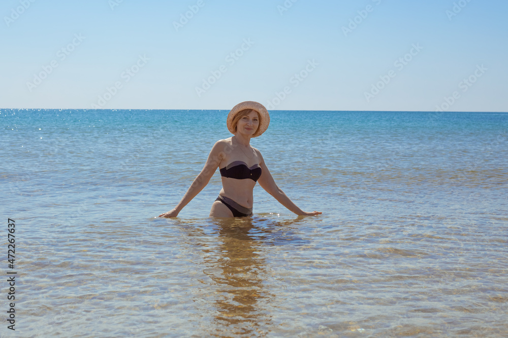 European woman in swimsuit and waist-length hat in the sea smiles and looks into the camera. Vacation on the seaside European woman in swimsuit and waist-length hat in the sea smiles and looks into the camera. Vacation on the seaside