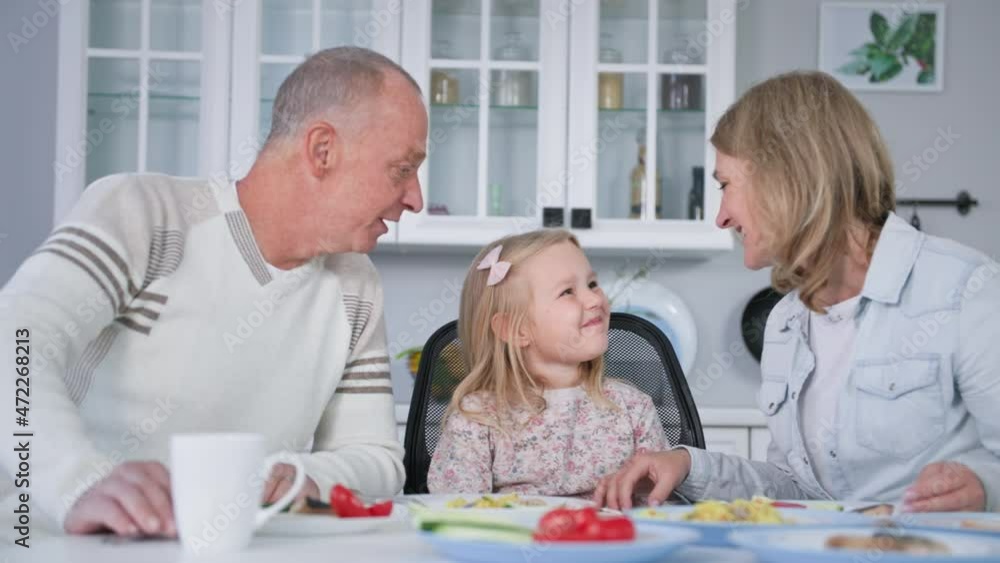 portrait of happy and friendly family with a small female child talking cutely to each other during a joint dinner in kitchen at table portrait of happy and friendly family with a small female child talking cutely to each other during a joint dinner in kitchen at table