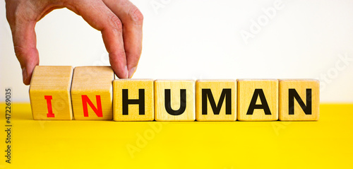 Human or inhuman symbol. Businessman turns wooden cubes and changes the word inhuman to human. Beautiful yellow table white background, copy space. Business, human or inhuman concept.