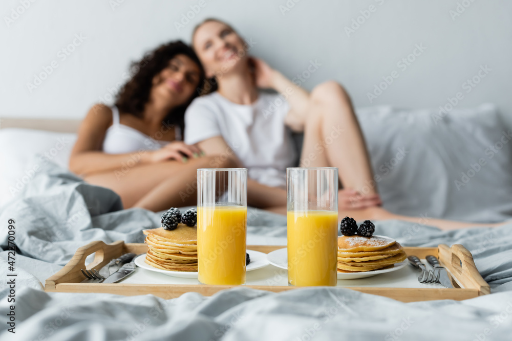 glasses with orange juice and pancakes on tray near blurred lesbian couple
