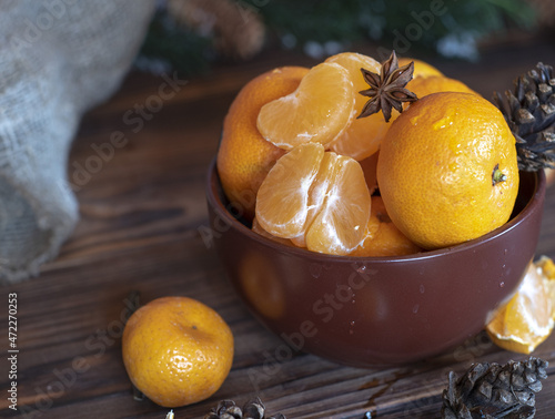 Ripe bright tangerines in a brown ceramic bowl.