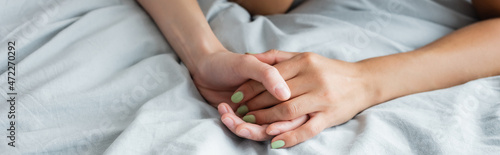 cropped view of young lesbian women holding hands on bed, banner