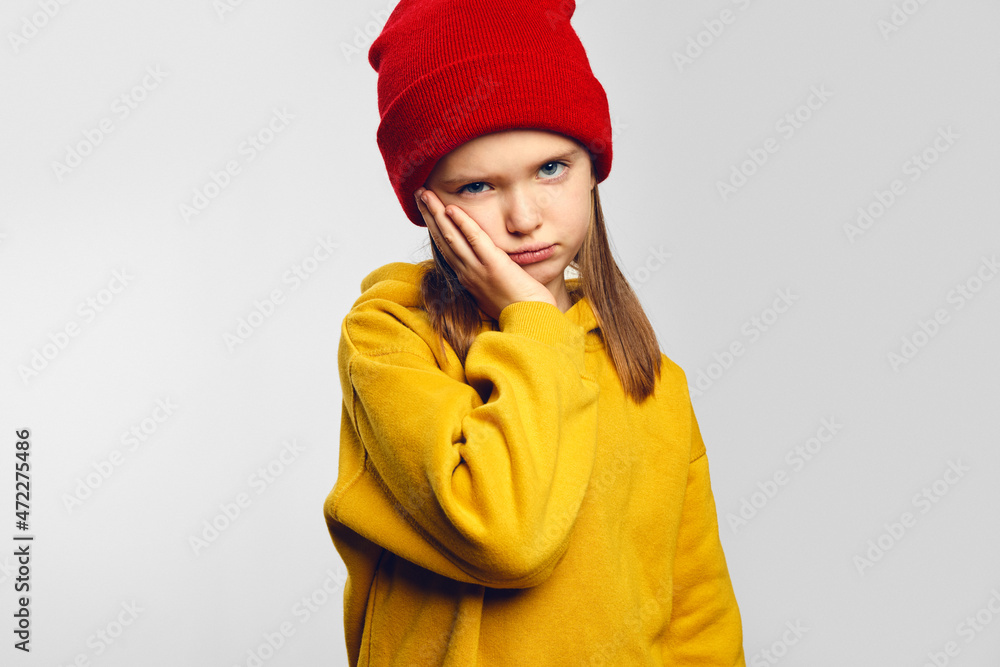 Hipster kid makes face palm has gloomy expression wears yellow hoodie and red hat, isolated over white background feels tired wants to sleep Hipster kid makes face palm has gloomy expression wears yellow hoodie and red hat, isolated over white background feels tired wants to sleep