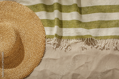Striped linen beach towel with fringes and straw hat on sandy beach with shadows from palm tree. Relaxation and tropical summer holidays concept photo