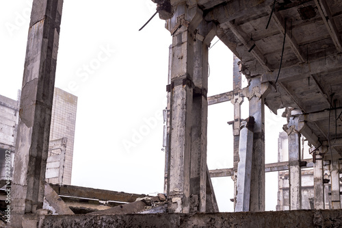 A row of huge concrete piles in a row of the frame of a destroyed building against a gray sky in a haze and the remains of the building. Background
