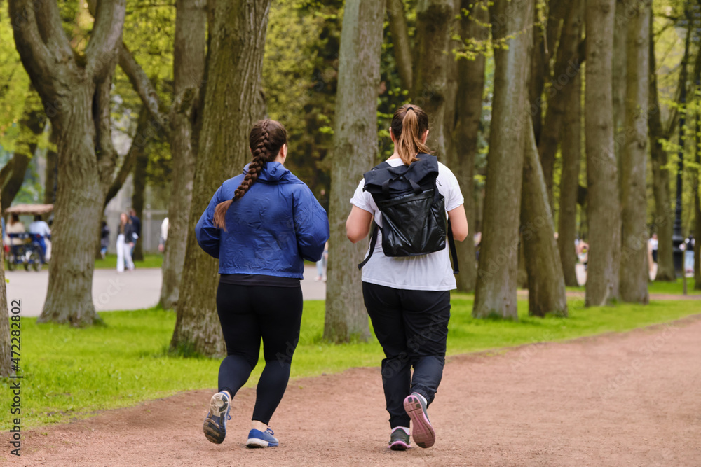 Fototapeta premium Two plump women are running through the park. Overweight girls go in for sports. Active lifestyle for weight loss.