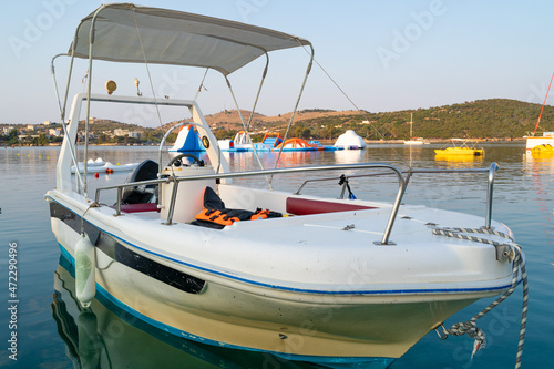 White motor boat in the blue sea water with some pedal boats and water slides in the background