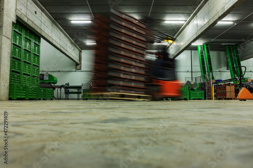 A forklift on the move. Warehouse and warehouse for packaging and stocks of goods. Forklifts is in an empty warehouse, in the background are boxes and pallets for packing fresh fruits and vegetables