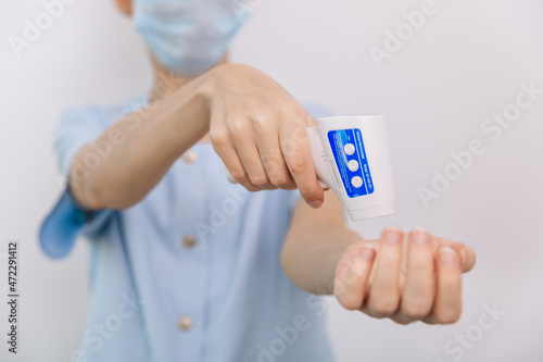 Temperature measurement gun in doctor hands. Close-up shot of doctor wearing protective surgical mask ready to use infrared isometric thermometer gun to check body temperature for virus symptoms
