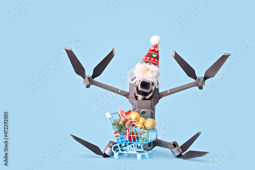 Drone in Santa's cap and a trolley cart with festive Christmas decor on the light blue background. Creative Christmas concept