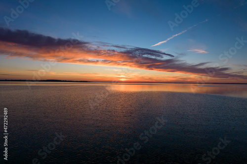 Beautiful sundown over the lake. Blue sky and pastel orange sun. Mirror image of clouds in the water.