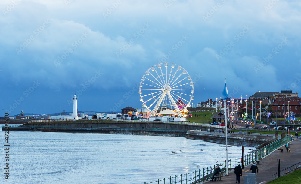 Dramatic sky over Seaburn Bay with ferris wheel and lighthouse.