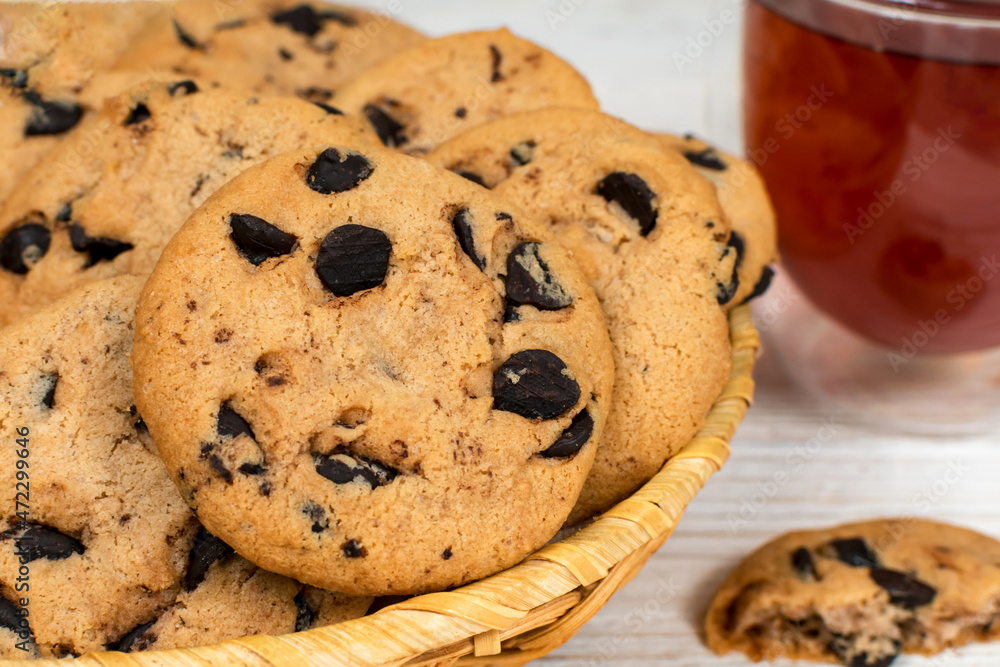 Chocolate cookies in a basket on the background of a glass cup of tea. Close-up. Chocolate cookies in a basket on the background of a glass cup of tea. Close-up.