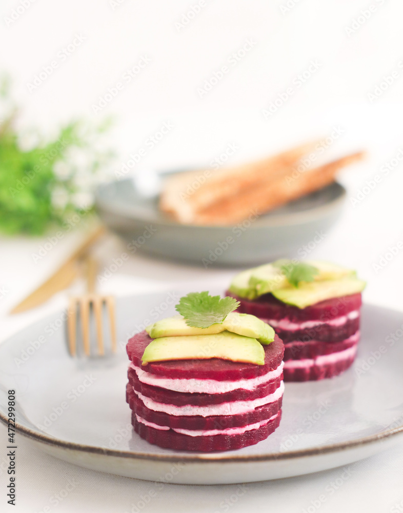 A plate layer of beetroot napoleon and goat cheese appetizer in plate topped with sliced avocado, shape as French mille-feuille a healthy dish and ideal for diet A plate layer of beetroot napoleon and goat cheese appetizer in plate topped with sliced avocado, shape as French mille-feuille a healthy dish and ideal for diet