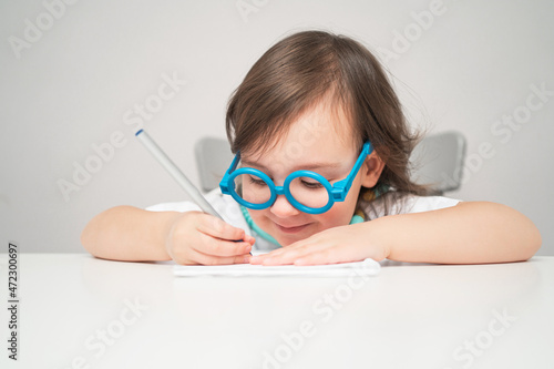 the child plays doctor. a girl in toy blue glasses sits at a white table. space for text and advertising. a girl in a white T-shirt smiles and looks straight