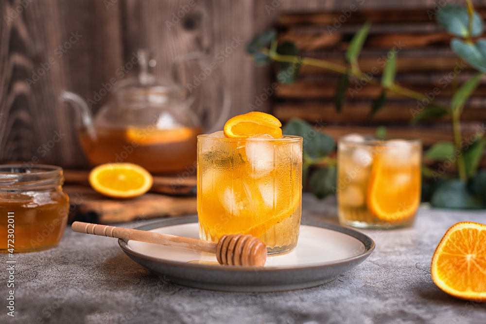 summer tea party: refreshing cold black tea with oranges and honey on a gray background summer tea party: refreshing cold black tea with oranges and honey on a gray background