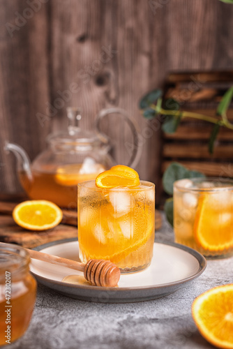 summer tea party: refreshing cold black tea with oranges and honey on a gray background